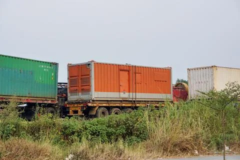 Several interregional cargo container transport trucks parked near a bushy area Stock Photos
