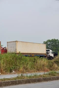 Several interregional cargo container transport trucks parked near a bushy area Stock Photos