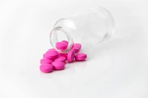 Several large bright pink tablets poured from a glass jar on a glossy white b Stock Photos