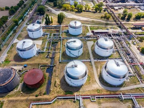 Several large circular tanks for storing oil are seen in an industrial settin Stock Photos
