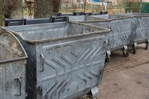 Several large, metallic garbage containers stand side by side on a paved su.. Stockfoto's