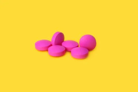 Several large pink tablets scattered on a yellow background. Stock Photos