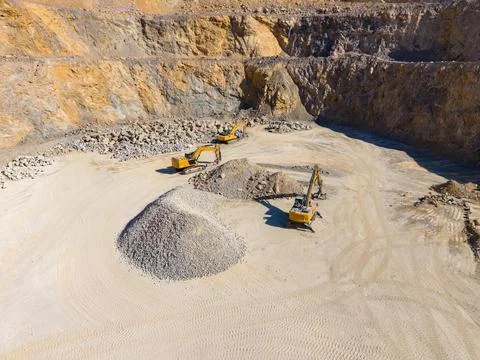Several machines operate in a quarry, digging and moving piles of rocks and d Stock Photos