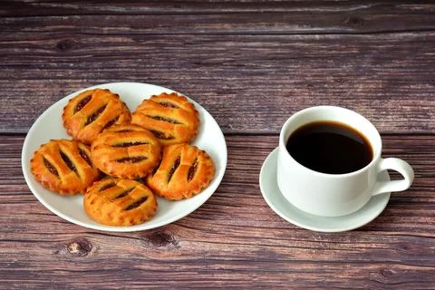 Several mini pies with apple jam in a round plate and a cup of black coffee.. Stock Photos