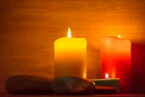 Several multi-colored candles are lit and surrounded by stones. Stock-Fotos