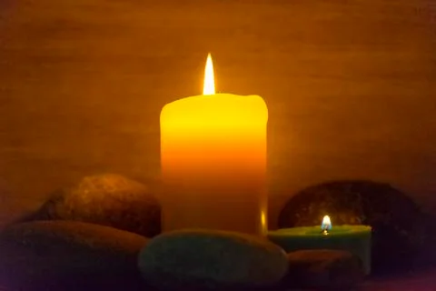Several multi-colored candles are lit and surrounded by stones. Stock Photos