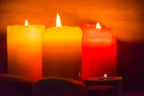 Several multi-colored candles are lit and surrounded by stones. 스톡 사진