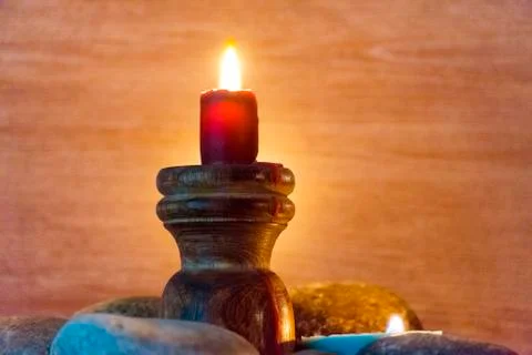 Several multi-colored candles are lit and surrounded by stones. 스톡 사진