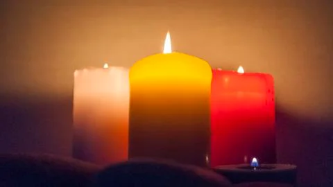 Several multi-colored candles are lit and surrounded by stones. Stock Photos