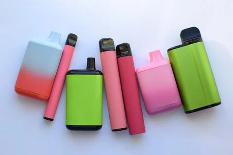 Several multi-colored electronic cigarettes lie on a light table. Stock Photos