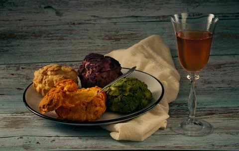 Several multi-colored profiteroles of cakes on a ceramic plate and a glass of Stock Photos