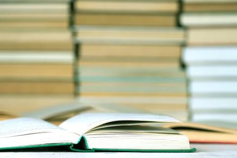Several open books on a table in front of a multitude of stacked books Stock Photos