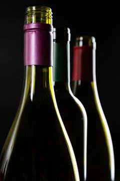 Several open Bottles of wine are in a row on a dark glossy background. Stock Photos