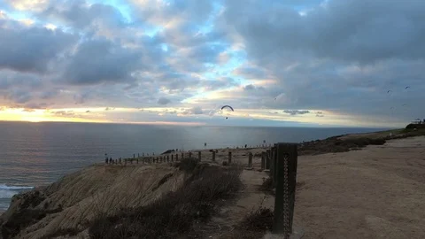 Several Paragliders fly past cliffs and circle over ocean under a cloudy sky Stock Footage 82104325