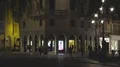 Several people walking by modern building with many arches down street at night HD Footage