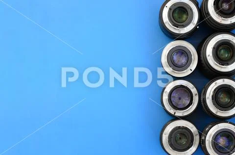 Several photographic lenses lie on a bright blue background. Space for text Stock Photos