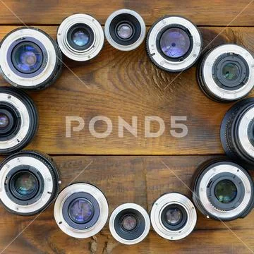 Several photographic lenses lie on a brown wooden background. Space for text Stock Photos