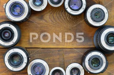 Several photographic lenses lie on a brown wooden background. Space for text Stock Photos