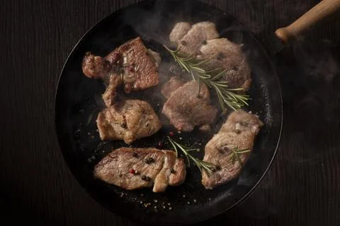 Several pieces of cooked beef steak sizzling in a black cast iron skillet Foto stock
