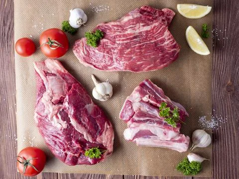 Several pieces of raw marbled black Angus beef lie on parchment surrounded by Stock Photos