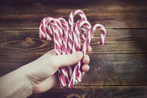 Several red and white candy canes in human hand on background of brown wood Stock Photos