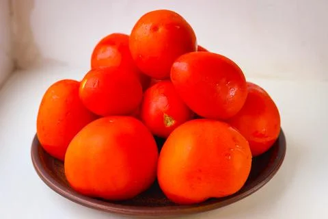 Several red tomatoes laid out on a clay plate stand on a white background Stock Photos
