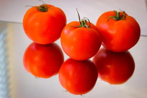 Several red tomatoes on a mirror surface Stock Photos