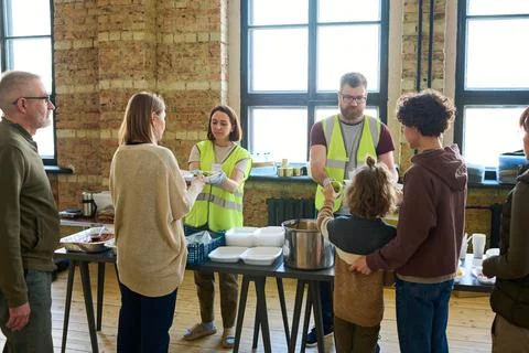 Several refugees standing by table with cooked food in front of volunteers Stock Photos