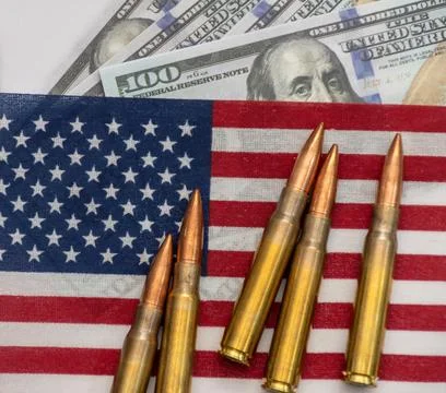 Several rifle bullets placed on a small United States flag with hundred dolla Stock Photos