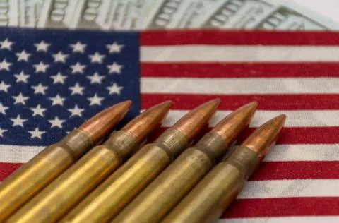 Several rifle bullets placed on a small United States flag with hundred dolla Stock Photos