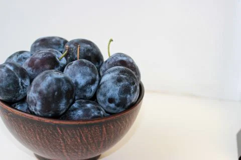 Several ripe blue plums in a deep clay plate on a white background with a cop Stock Photos