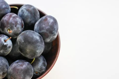 Several ripe blue plums in a deep clay plate on a white background with a cop Stock Photos