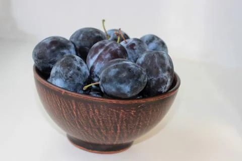 Several ripe blue plums in a deep clay plate on a white background with a cop Stock Photos