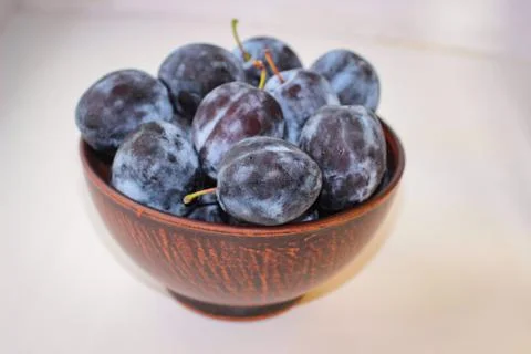 Several ripe blue plums in a deep clay plate on a white background with a cop Stock Photos