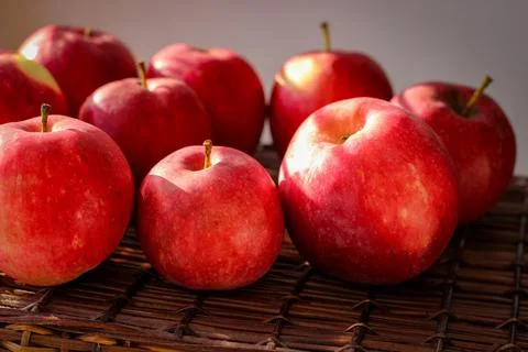 Several ripe red apples stand on a wicker basket illuminated by rays of the s Stock Photos