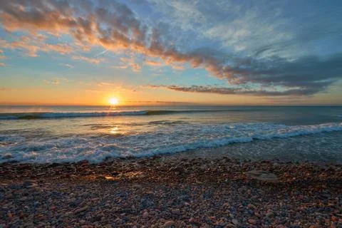 Several rocks on the beach in the warm light of a sunrise Stock Photos