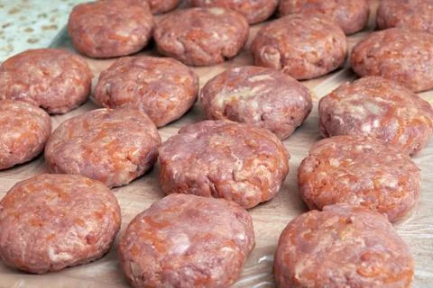 Several rows and lines of fresh not fried cutlets lie on the Board. Stock Photos