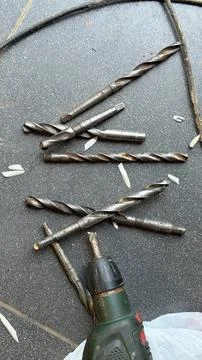 Several rusty metal drill bits of various sizes lying on a dark tiled surface Stock Photos