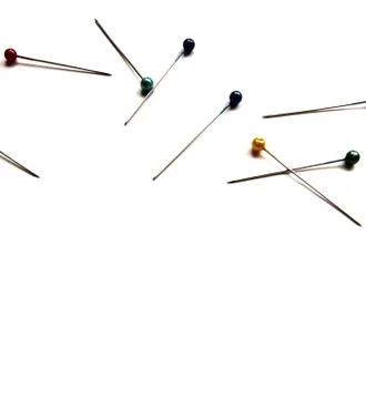 Several sewing pins with colored beads lie on a white isolated background. Stock Photos