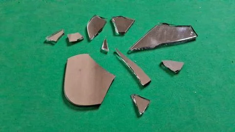 Several sharp shards of broken mirror resting on bright green paper Stockfoto's
