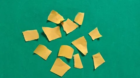 Several small torn yellow paper pieces on vibrant green background Stock Photos