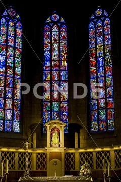 Several tall stained glass church windows with statue of Virgin Mary and Child Stock Photos