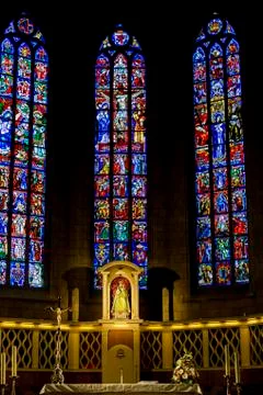 Several tall stained glass church windows with statue of Virgin Mary and Child Stock Photos