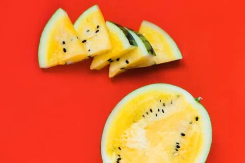 Several triangular pieces and half of ripe yellow watermelon on a red backgro Stock Photos