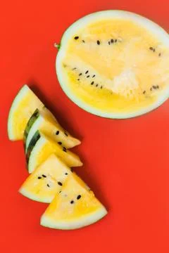 Several triangular pieces and half of ripe yellow watermelon on a red backgro 스톡 사진