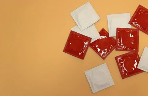 Several unopened red and white condoms on orange background Foto stock