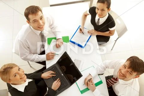 Several white collar workers looking upwards at camera from their workplaces Stock Photos