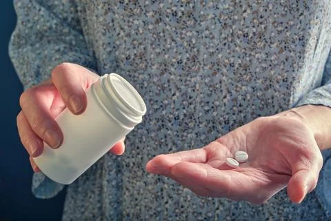 Several white round tablets (vitamins) on a woman's palm, a white plastic b.. 스톡 사진