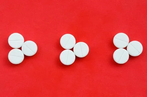 Several white tablets lie on a bright red background in the form of three tri Foto stock