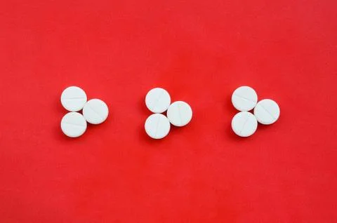 Several white tablets lie on a bright red background in the form of three tri Foto stock